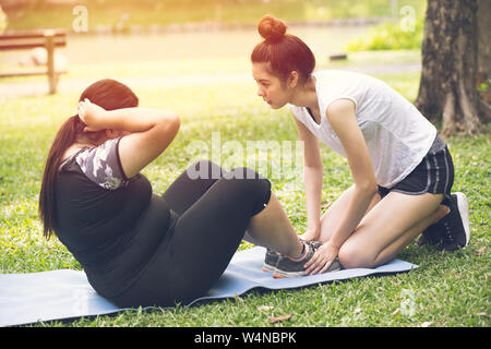 Personal trainer coach teen aiutare la formazione di grassi amico ragazza di esercitare la dieta per un sano all'aperto nel parco Foto Stock