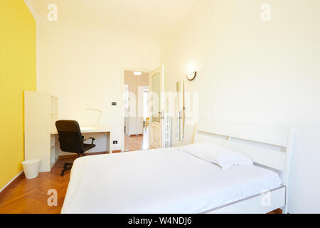 Interiore camera da letto in appartamento ristrutturato con pavimento in parquet e parete gialla Foto Stock