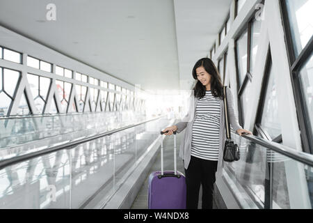 Asian donna incinta in piedi tirando la valigia Foto Stock