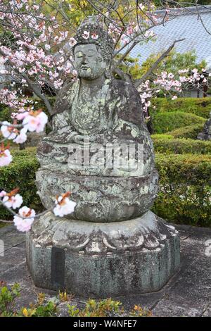 Statua di Buddha - antica scultura in pietra e fiori di ciliegio fiori a Ninna-ji il tempio di Kyoto, Giappone. Foto Stock