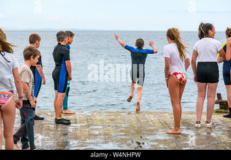 A North Berwick, East Lothian, Scozia, Regno Unito, 24 luglio 2019. Regno Unito Meteo: ragazzi e ragazze locali trattare con la canicola estiva che salta fuori il vecchio molo nel Firth of Forth per raffreddarsi Foto Stock