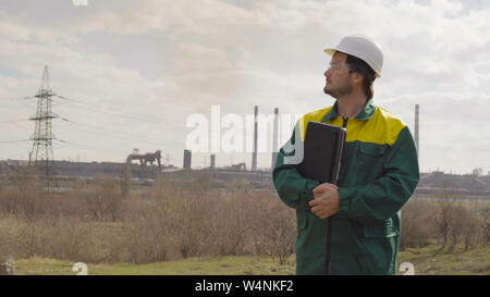 Il maschio di progetti tecnici i lavori. Giornata di sole e nuvole. L'uomo è vestito in un verde giubbotto di occhiali da sole Foto Stock