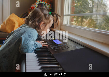 Una bambina curiosamente esplora i tasti su una tastiera di pianoforte Foto Stock