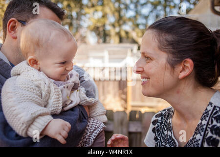 Un happy baby sorrisi a madre mentre viene mantenuto in padre di braccia Foto Stock