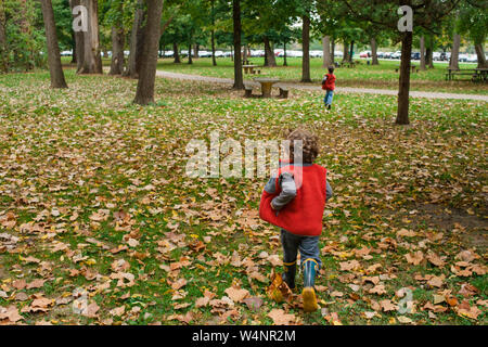 Due piccoli bambini corrono insieme attraverso foglie cadute in un parco Foto Stock