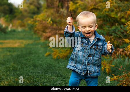 Un Laughing baby boy detiene il bastone in mano e gioca fuori in autunno Foto Stock