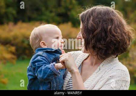 Un sorridenti madre detiene il suo bambino in braccio al di fuori Foto Stock