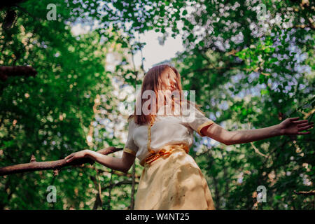 Donna in piedi su un albero in un abito giallo Foto Stock