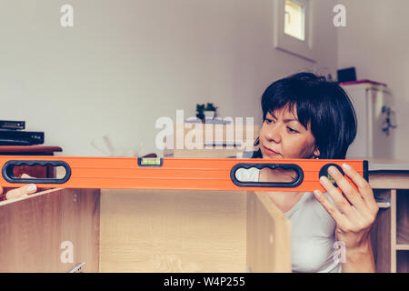 Donna di assemblaggio di mobili nuovi e utilizzando lo strumento di allineamento. Foto Stock