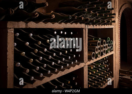 Polverose bottiglie di spumante vino spumante disposte in righe sul ripiano di legno nella cantina di produzione nella regione di Penedes, Catalogna, Spagna Foto Stock