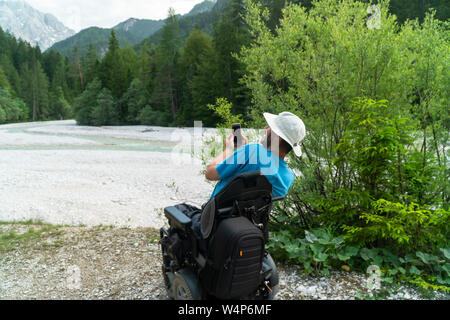 Uomo sulla sedia elettrica utilizzando la fotocamera dello smartphone in natura Foto Stock