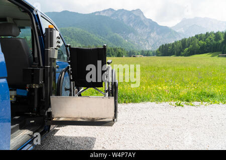 Il nero di sollevamento elettrico veicolo specializzato per le persone con disabilità. Sedia a rotelle vuota su una rampa con la natura e le montagne nella parte posteriore Foto Stock