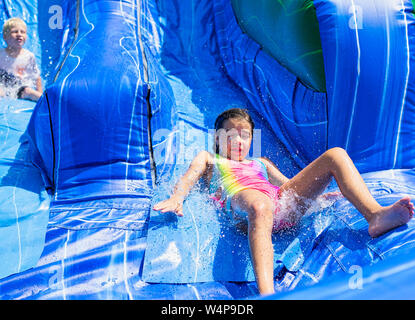 Lo sguardo sul volto dice tutto come i bambini di venire giù gli scivoli acquatici per rinfrescarsi nelle calde giornate estive di Alabama. Foto Stock