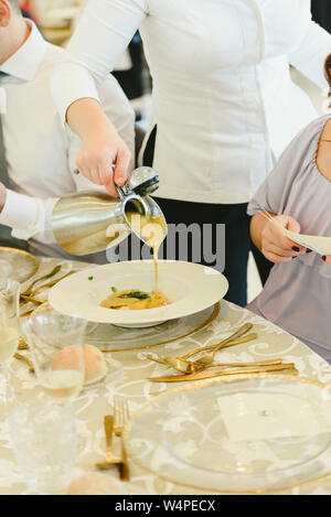 Un cameriere versa la salsa su un piatto di carne in un ristorante elegante. Foto Stock