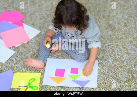 Carino bambina fare applique, colle casa colorati, applicando una carta a colori utilizzando colla stick mentre facendo arti e mestieri in età prescolare o home. L'id Foto Stock