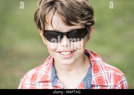 Ragazzo, dieci anni, con occhiali da sole e plaid shirt guardando sorridente, Ritratto, Germania Foto Stock