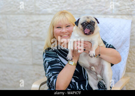 Sorridenti donna matura con cane all'aperto.Felice medioevo donna giocando con il bulldog sul cortile nella luce del tramonto, vacanze estive. Signora con f Foto Stock