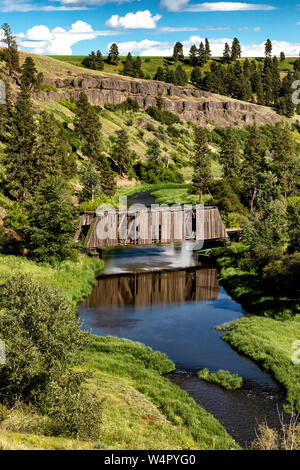 La riflessione di un vecchio ponte coperto attraversando un piccolo fiume. Foto Stock