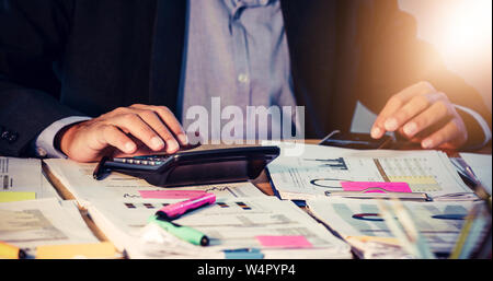 Gli imprenditori asiatici sono uso di calcolatrici per l'analisi dei documenti di progetto grafico e lo schema finanziario che funziona in background sul tavolo per ufficio Foto Stock