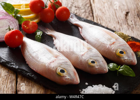 Non cotti dorado o orata Orate di mare Pesce con spezie, pomodoro, cipolla e limone close up su una scheda di ardesia sul tavolo orizzontale. Foto Stock