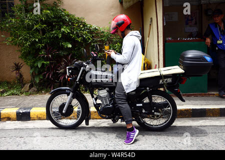 ANTIPOLO City, Filippine - Luglio 23, 2019: un motociclo conducente si ferma in corrispondenza di un marciapiede per controllare sul suo smartphone. Foto Stock