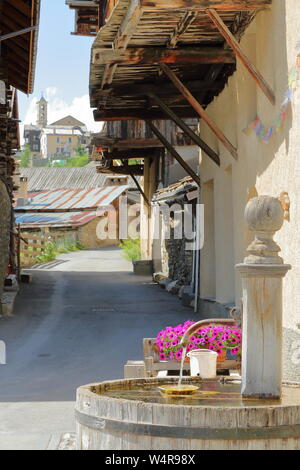 Un tradizionale fontana di legno tradizionale con balconi in legno e la chiesa in background in Saint Veran village, Queyras parco naturale, Francia Foto Stock