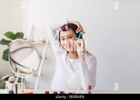 Tutorial di acconciatura. Donna asiatica spazzolare i capelli e sorridente piacevolmente durante le riprese di un tutorial per la sua bellezza blog Foto Stock