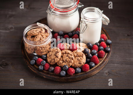 Piastra in legno pieno di delicios e gustosi biscotti accanto a bluebarries fresco. Fresk latte per i cookie. Foto Stock