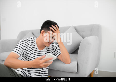 Unico Uomo triste controllo telefono cellulare seduta sul pavimento nel salotto di casa Foto Stock