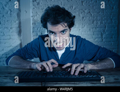 Addict giovane uomo da soli di notte sul computer portatile sensazione stressato e sopraffatto cercando di completare il lavoro o il premiato gioco online o il gioco d'azzardo. In worka Foto Stock