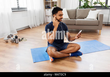 Uomo indiano con lo smartphone sul tappeto di esercizio a casa Foto Stock