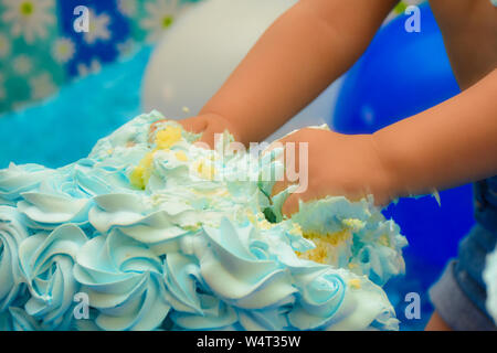 Un irriconoscibile bambino smashing torta di compleanno con le mani. Torta di compleanno smash da ragazzino concetto. Foto Stock