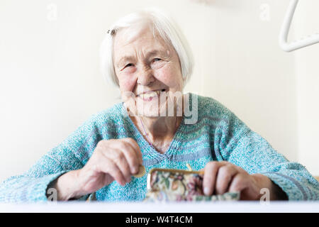 Allegro anziani 96 anni donna seduta al tavolo a casa felice con la sua pensione risparmi nel suo portafoglio dopo il pagamento di fatture. Foto Stock