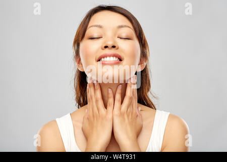 Sorridenti giovane donna asiatica di toccare il suo volto Foto Stock