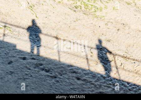 Le ombre proiettate nel fango con la bassa marea da due persone in piedi sulla banchina a Bideford, Devon, Regno Unito Foto Stock