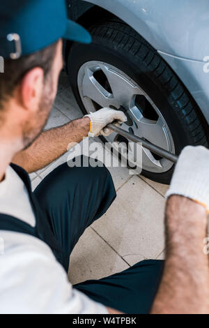 Vista ritagliata della meccanico di automobili in uniforme tenendo la chiave metallica vicino auto Foto Stock