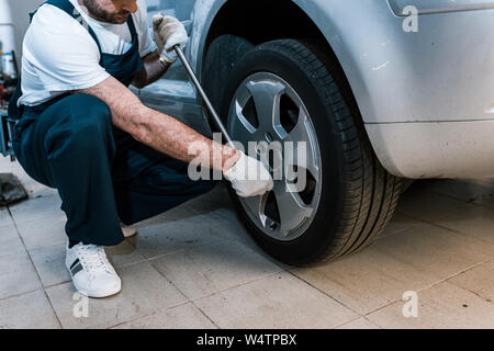 Vista ritagliata della meccanico automatico in uniforme tenendo la chiave metallica vicino auto Foto Stock