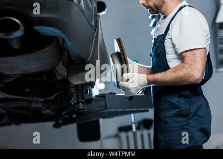 Vista ritagliata della meccanica auto riparazione automobile e tenendo premuto il freno per auto Foto Stock