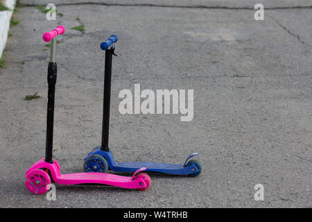 Due scooter senza figli, rosa per le bambine e blu per il ragazzo sulla strada Foto Stock