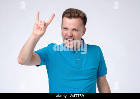 Giovane uomo bello urlando e facendo rock gesti con le mani mentre vi godete della musica. Foto Stock