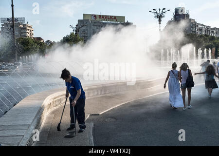 Piazza Unirii, Bucarest, Romania. Come parte delle spettacolari fontane, un appannamento di acqua sistema raffredda i passanti durante il soffocante calore estivo Foto Stock