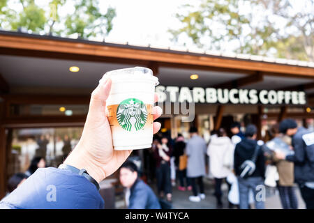 Tokyo, Giappone - 17 Marzo 2019: mano azienda Starbucks Coffee Cup con il logo del marchio nella parte anteriore del caffè Starbucks Onshi Ueno Park durante la rosa ciliegia bloss Foto Stock