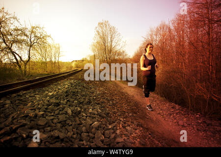 Bambina corre sulla strada lungo le piste e il tramonto Foto Stock