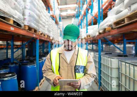 Lavoratore di sesso maschile il controllo delle scorte su tavoletta digitale in magazzino Foto Stock