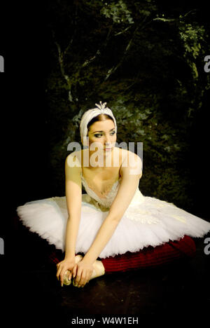 Ballerina durante una pausa in una prova generale in tutù bianco e rosso scalda la gamba. Foto Stock