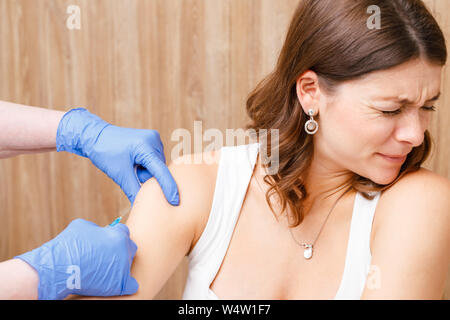 La donna ha paura della siringa ruotando la sua testa fuori la spremitura gli occhi per la paura. Assistente medico dando una iniezione intramuscolare di un vaccino per il suo braccio Foto Stock