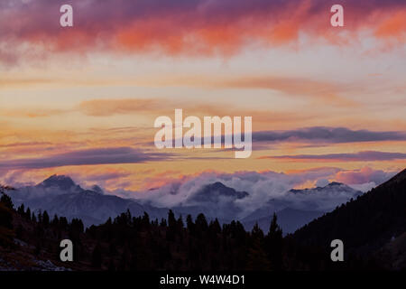 Panorama della foresta di silhouette e cime di montagna in rosso arancio blu gradiente di nuvole al tramonto. Foto Stock