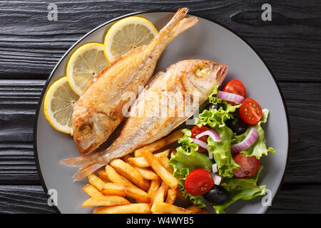 Rosa fritto dorado servito pesce con patatine fritte e insalata di verdure close-up su una piastra sul tavolo. parte superiore orizzontale vista da sopra Foto Stock