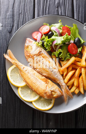 Rosa fritto dorado servito pesce con patatine fritte e insalata di verdure close-up su una piastra sul tavolo. Verticale in alto vista da sopra Foto Stock