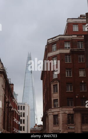 È possibile vedere un vecchio cercando casa rossastro nella parte anteriore del moderno grattacielo Shard in Londra, Regno Unito. Vecchio e nuovo crea un contrasto nella foto. Foto Stock